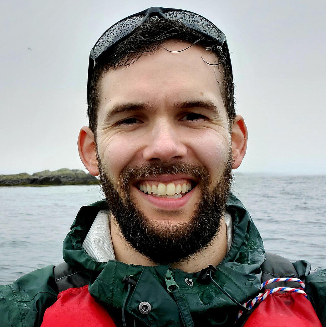 Evan Evan wearing a green rain jacket with the ocean in the background